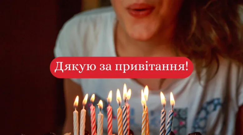 Чоловік дмухає свічки на торт з українським привітанням.