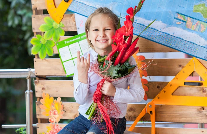 Дівчинка тримає червоні квіти та усміхається.